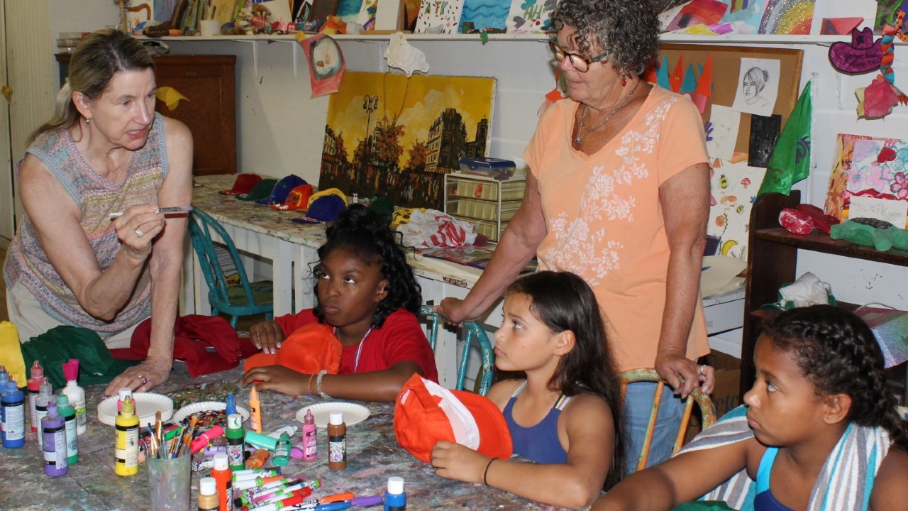 Geneva Lake Arts Foundation members Samantha Polek (standing, left) and Sarah McConnell provided instruction to campers Cayliae, Mikaila, and Amiyah before they decorated their caps during an art activity at Holiday Home Camp. Fred Noer photo